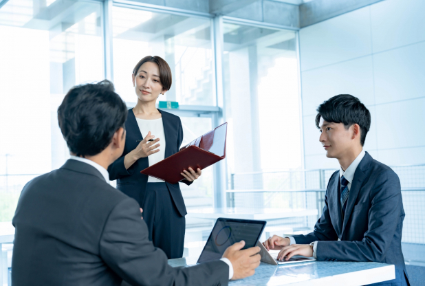 画像：ミーティングルームで打ち合わせをする3人の社員